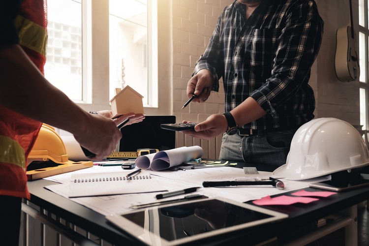 Two architects planning together at desk with blueprints. Photo chantier